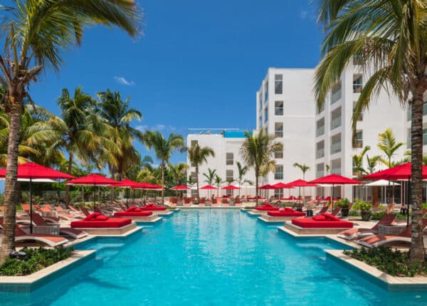 the blue pool at the s hotel with red umbrellas next to palm trees