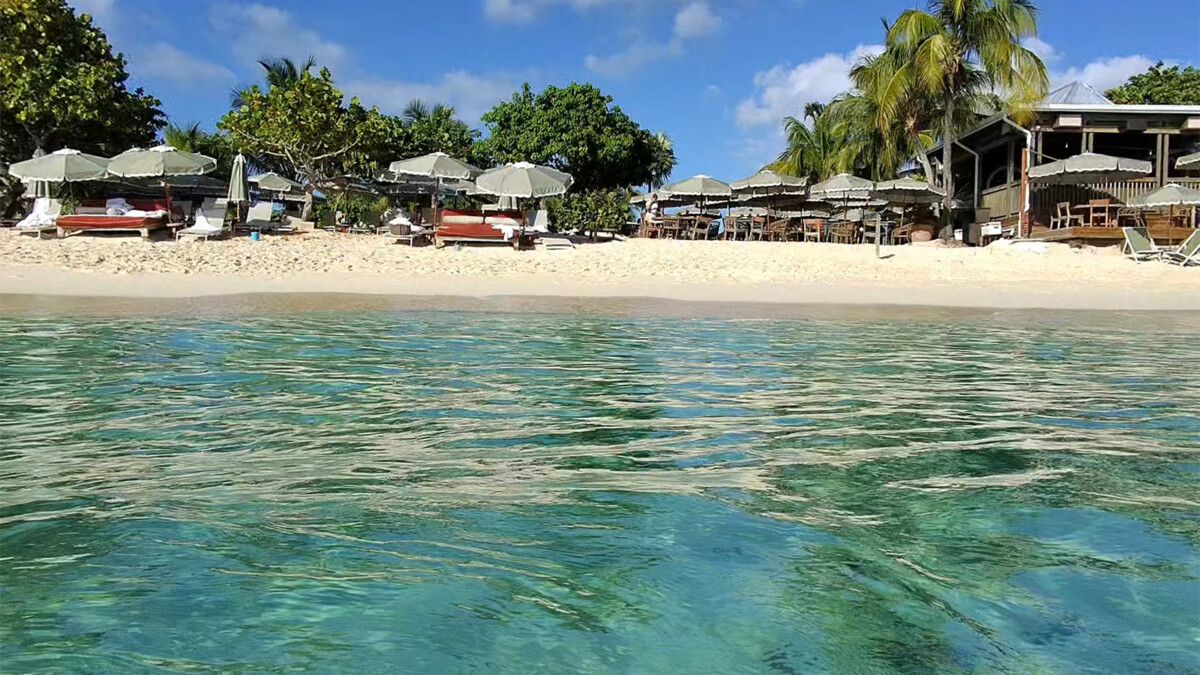 Emerald and turquoise water at Seven Mile Beach in Grand Cayman, with beach bars, umbrellas and palm trees along the shoreline